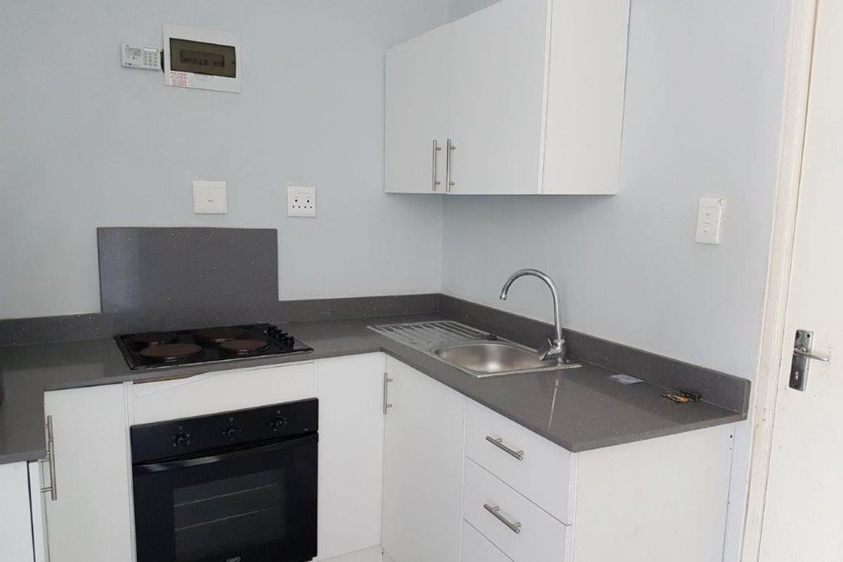 A clean, compact kitchen featuring white cabinetry, grey stone countertops, a built-in oven, electric hob, and a stainless steel sink.
