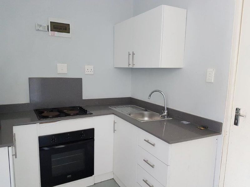 A clean, compact kitchen featuring white cabinetry, grey stone countertops, a built-in oven, electric hob, and a stainless steel sink.