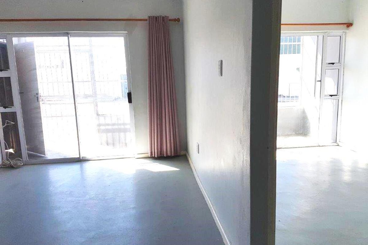An empty living area featuring concrete flooring and sliding glass doors leading to an outdoor space, requiring cosmetic updates.