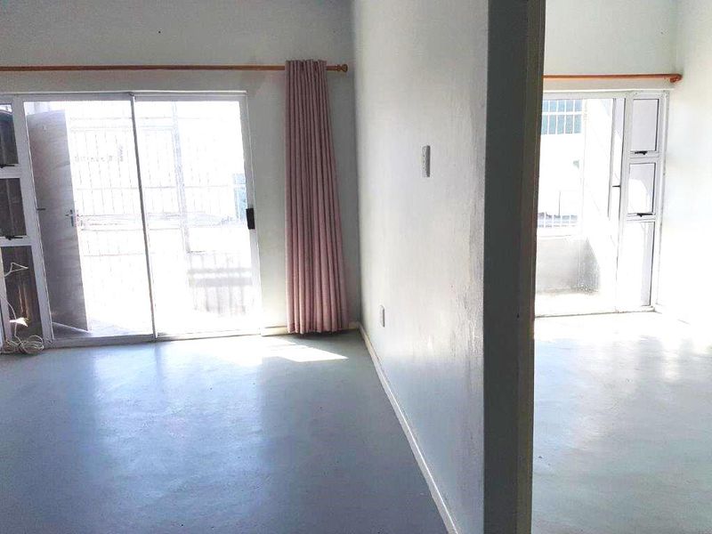 An empty living area featuring concrete flooring and sliding glass doors leading to an outdoor space, requiring cosmetic updates.