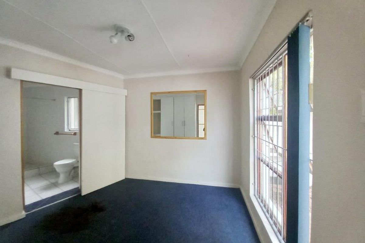 An empty bedroom featuring built-in cupboards, security bars on the window, and an en-suite bathroom access point.