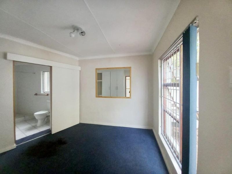 An empty bedroom featuring built-in cupboards, security bars on the window, and an en-suite bathroom access point.