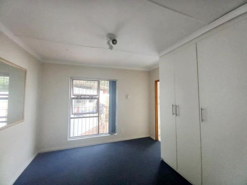 A clean, empty bedroom featuring built-in cupboards, carpeted flooring, and a window fitted with security bars.