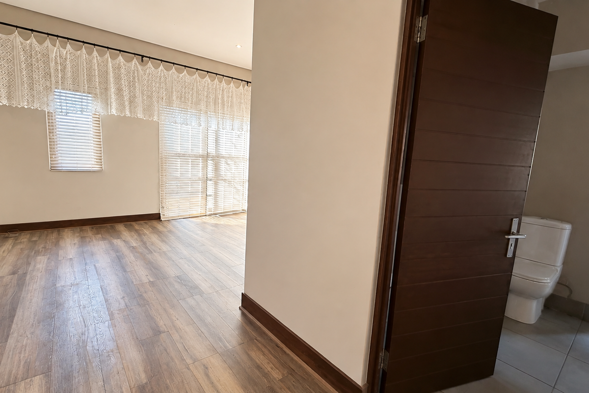 Spacious bedroom featuring laminate flooring, built-in cupboards, and an en-suite bathroom access, offering a clean and neutral living space.