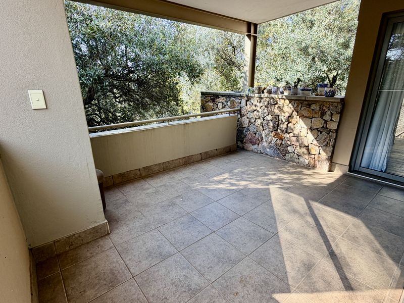 A spacious covered balcony featuring tiled flooring, a decorative stone-clad wall, and a metal railing, offering a pleasant outdoor space.