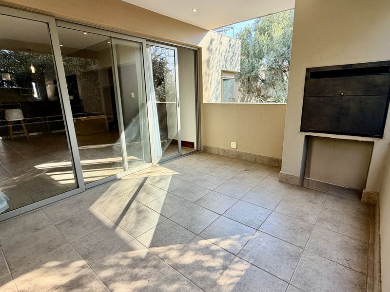 A spacious covered balcony featuring tiled flooring, a built-in braai, and large sliding glass doors providing seamless access to the interior living area.