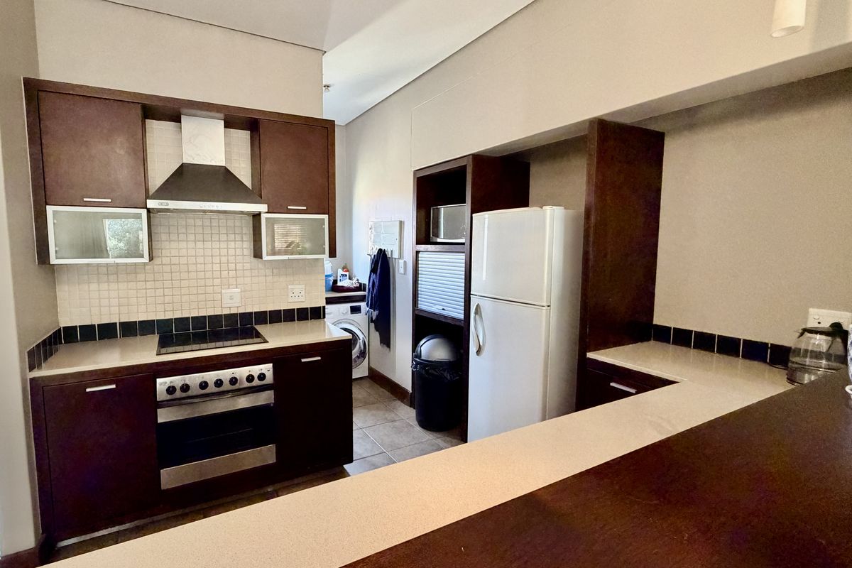 A functional kitchen featuring dark wood cabinetry, stone countertops, a breakfast bar, and integrated appliances including an oven and hob.