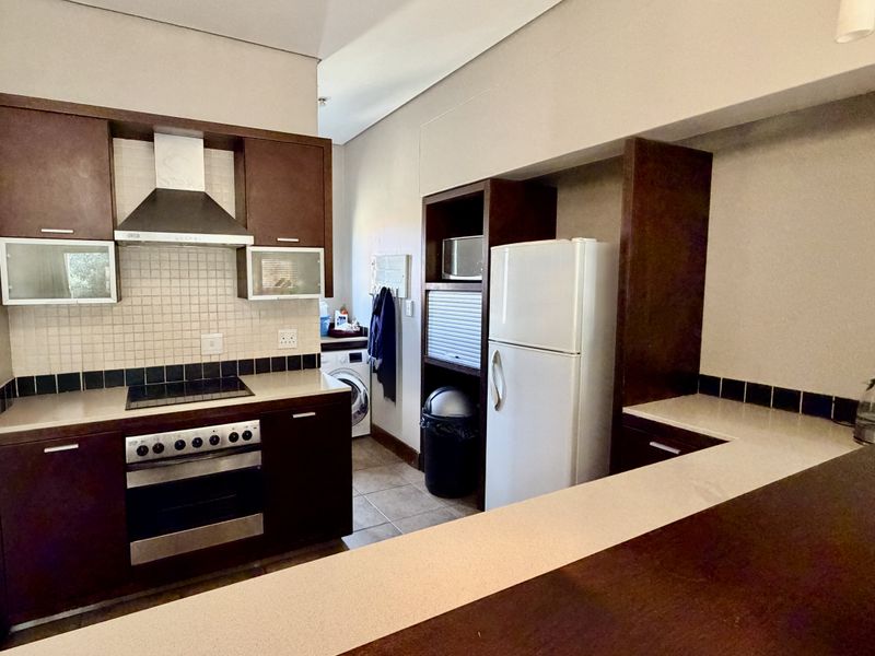 A functional kitchen featuring dark wood cabinetry, stone countertops, a breakfast bar, and integrated appliances including an oven and hob.