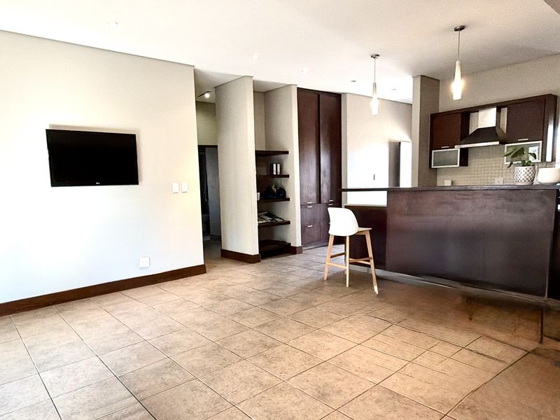 An open-plan living and kitchen area featuring tiled flooring, dark wood cabinetry, a breakfast bar, and modern recessed and pendant lighting.