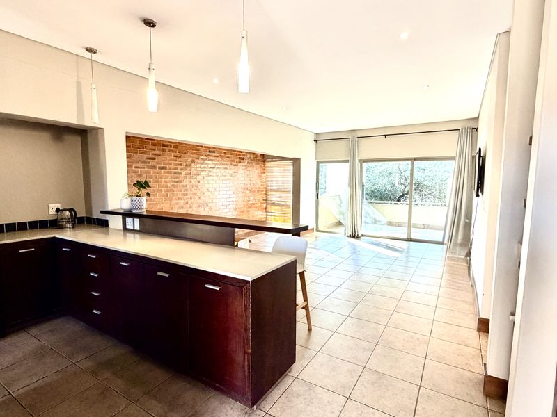 Spacious open-plan living area featuring a kitchen with breakfast bar, exposed brick accent wall, and large sliding doors leading to an outdoor space.