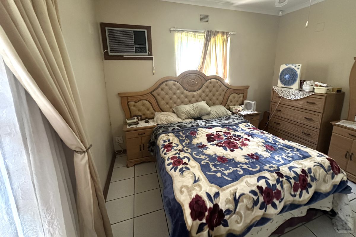 A bedroom featuring tiled flooring, a wall-mounted air conditioning unit, and a window with curtain fixtures.