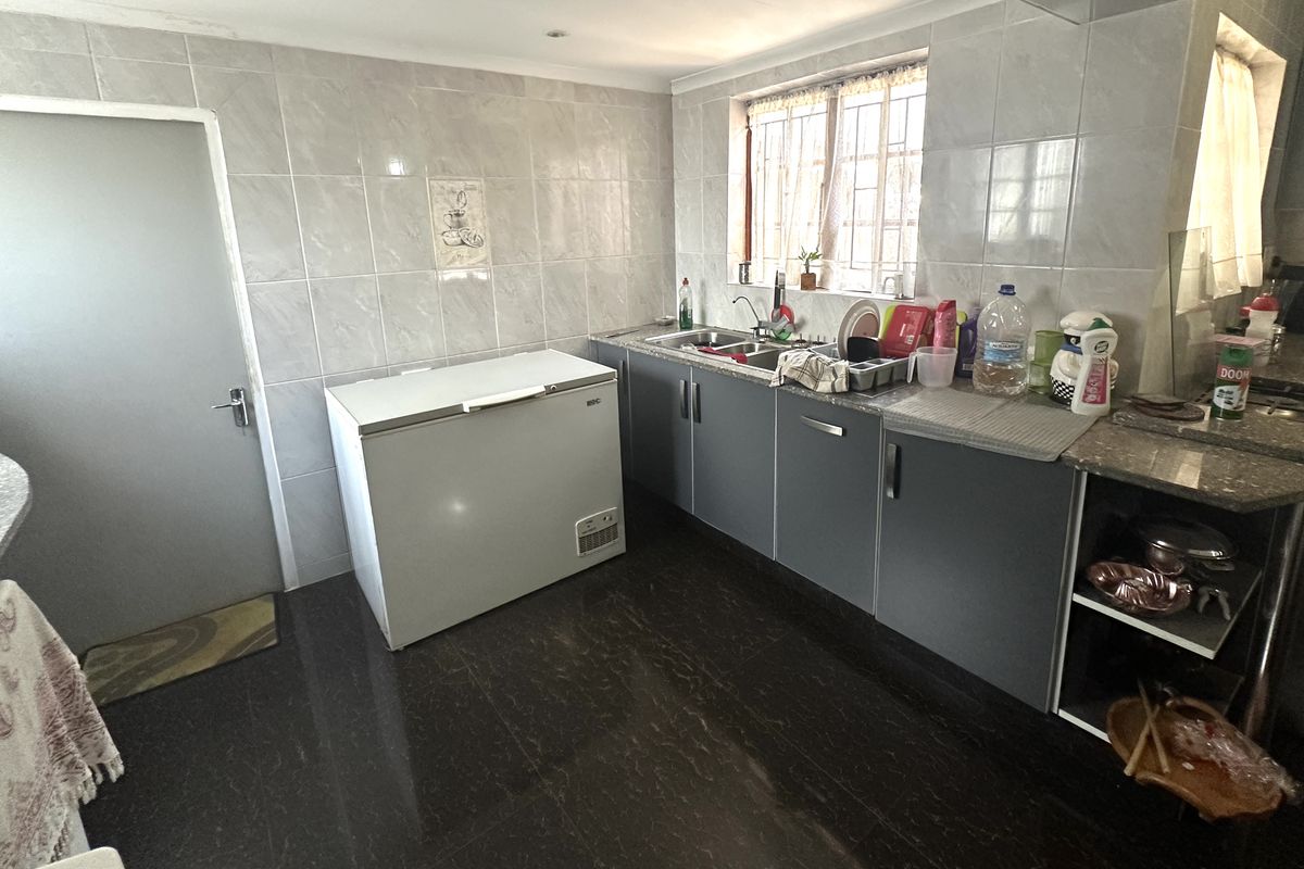 A functional kitchen featuring dark grey cabinetry, tiled walls, and dark flooring, providing a practical workspace with integrated sink and ample storage.