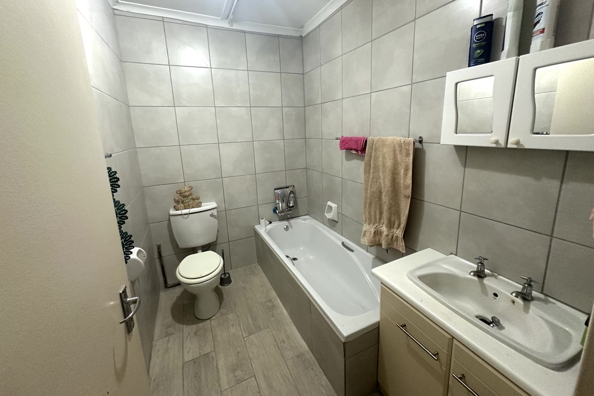 A functional bathroom featuring a built-in bathtub, vanity basin with storage, and wall-mounted medicine cabinet, finished with neutral floor-to-ceiling wall tiles.