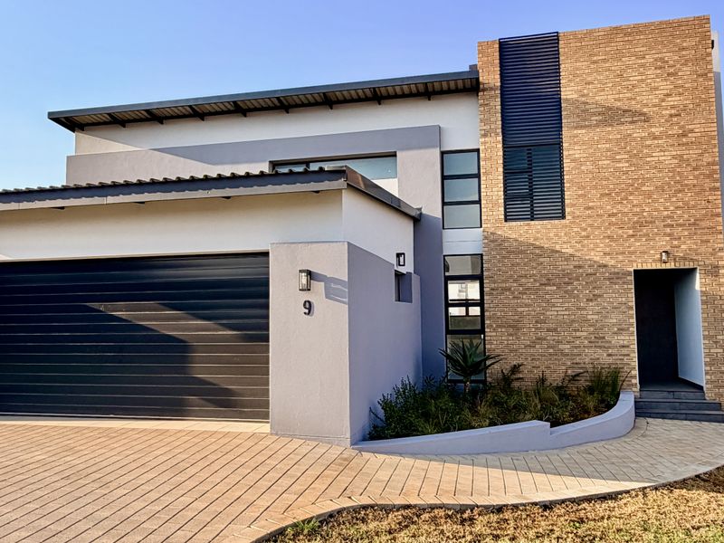 Modern double-story residential facade featuring a combination of brick and plastered finishes, a paved driveway, and an integrated garage.