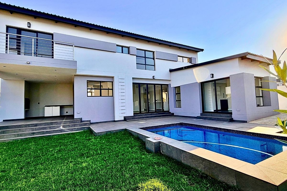 Rear view of a modern two-story home featuring a swimming pool, covered patio area, upper-level balcony, and landscaped lawn.
