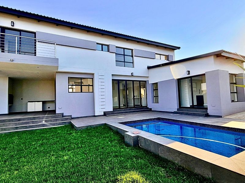 Rear view of a modern two-story home featuring a swimming pool, covered patio area, upper-level balcony, and landscaped lawn.