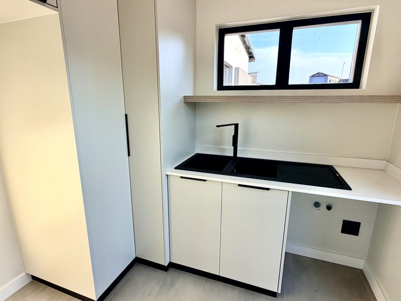 Modern scullery featuring clean white cabinetry, a double sink with black fixtures, and a floating shelf under a window.