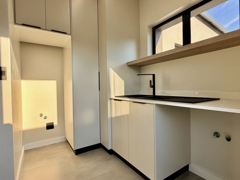 A modern, clean laundry room featuring built-in cabinetry, a sleek sink with black fixtures, and dedicated plumbing connections for appliances.