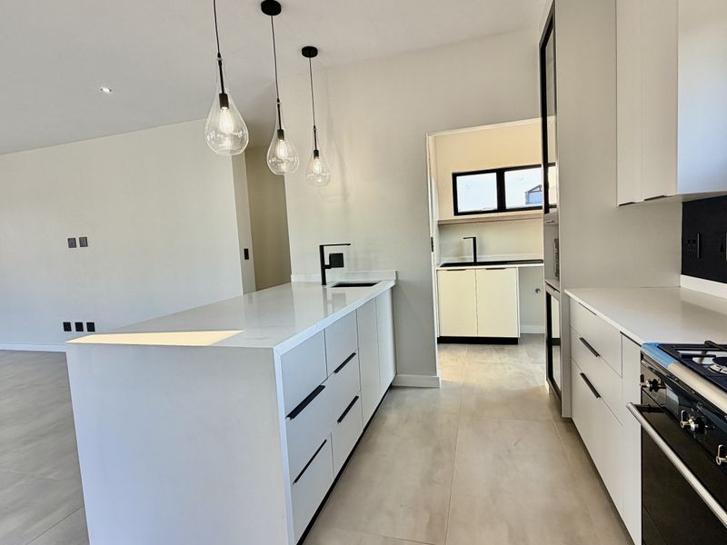 Modern open-plan kitchen featuring a central island, quartz countertops, gas stove, and an adjacent scullery area with neutral tiled flooring throughout.