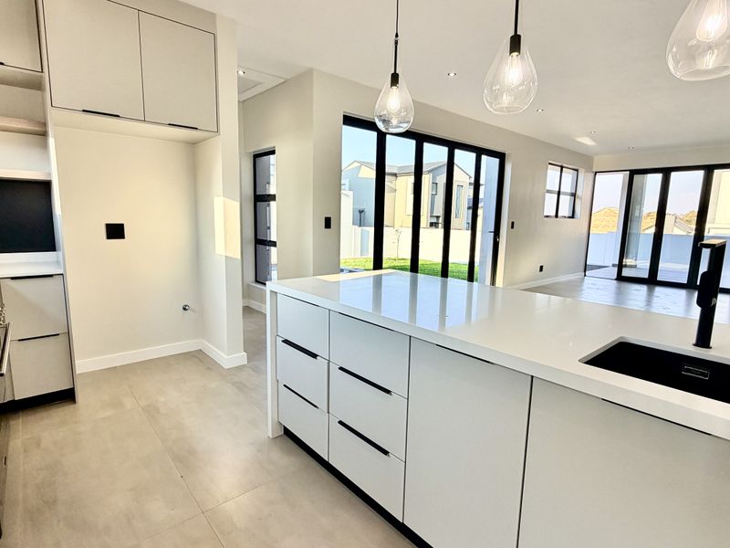 Modern open-plan kitchen featuring a central island with quartz countertops, gas hob, and sleek cabinetry, flowing seamlessly to the outdoor patio area.
