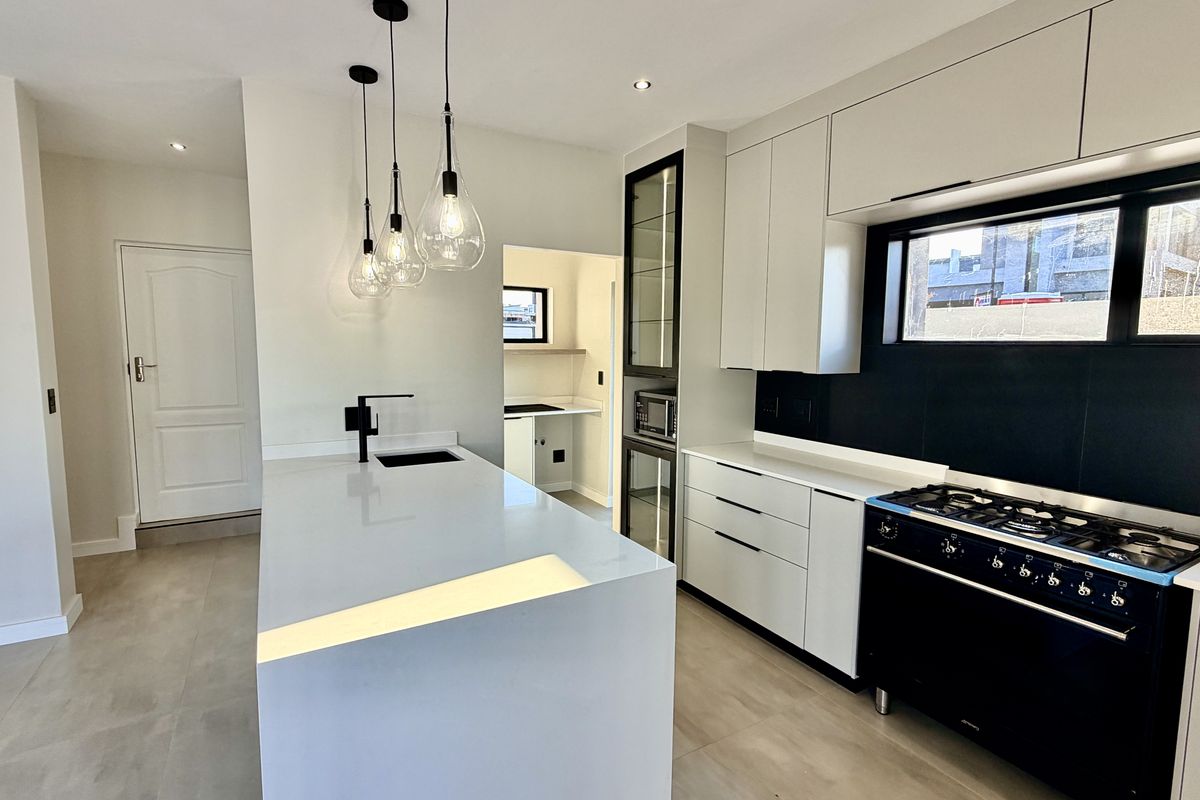 Modern kitchen featuring a central island with quartz countertops, sleek cabinetry, a gas stove, and an adjacent scullery area.