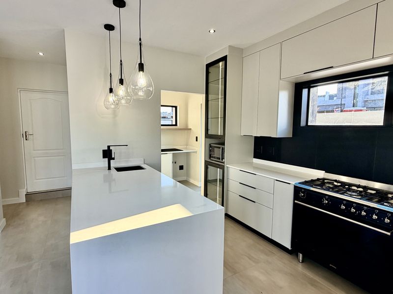 Modern kitchen featuring a central island with quartz countertops, sleek cabinetry, a gas stove, and an adjacent scullery area.