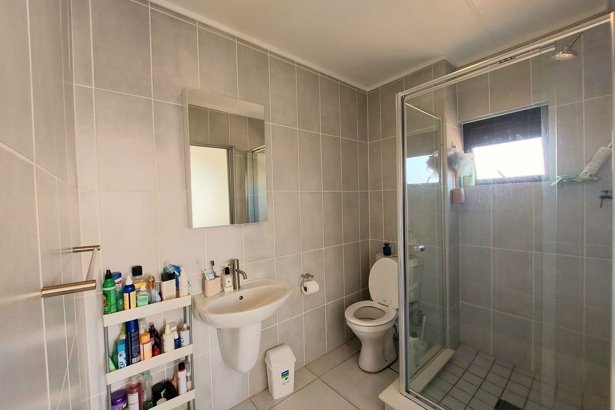 A functional bathroom featuring a pedestal basin, a glass-enclosed shower, and neutral wall and floor tiling.