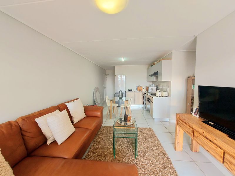 Open-plan living area featuring a compact kitchen with built-in cabinetry, oven, and extractor fan, seamlessly flowing into the lounge space with tiled flooring.