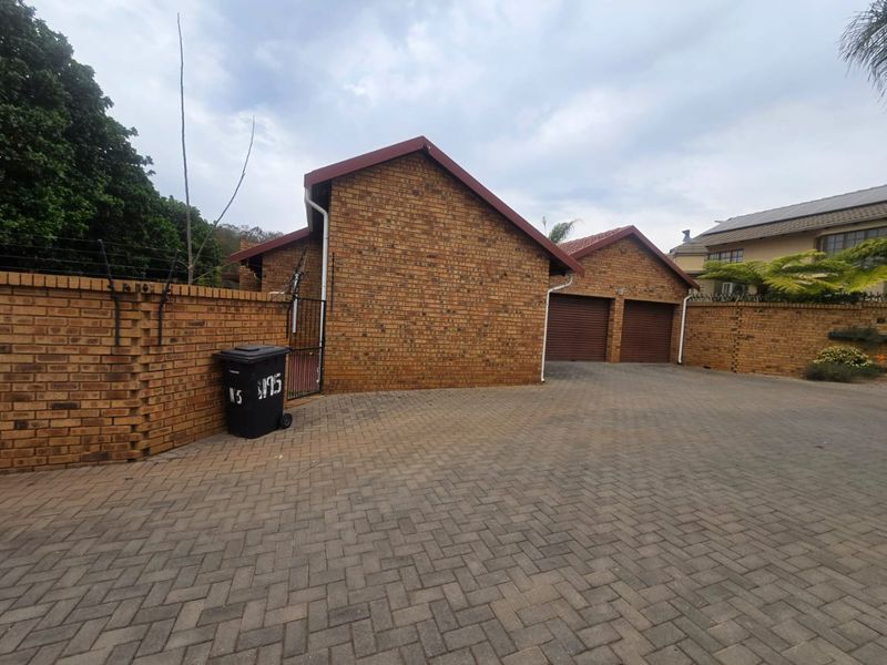 Exterior view of the property featuring a double garage, paved driveway, and secure brick perimeter wall with electric fencing.