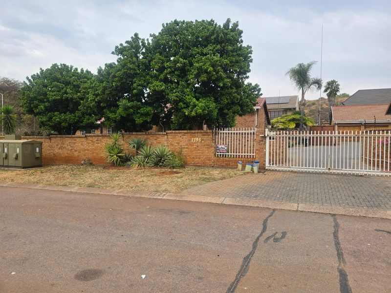 Front view of the property featuring a brick boundary wall, secure metal gate, and paved driveway access.