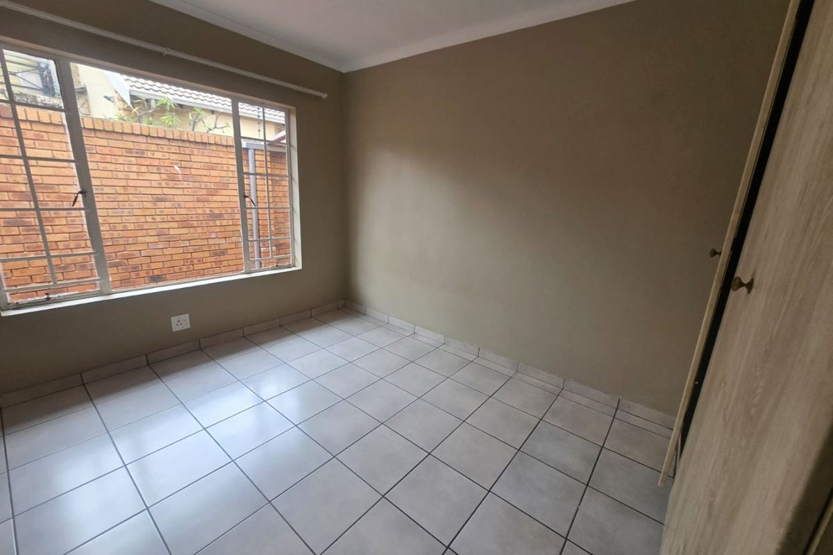 A clean, empty bedroom featuring neutral wall tones, tiled flooring, and a built-in cupboard with security bars on the window.