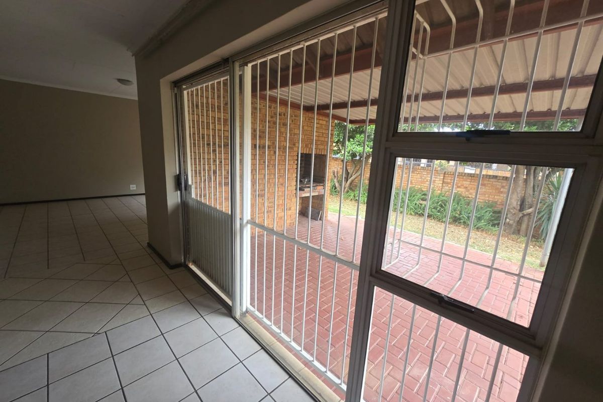 Spacious living area with tiled floors and large sliding doors opening onto a covered patio featuring a built-in braai and brick paving.