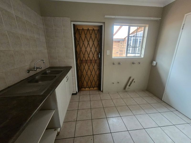 A functional laundry room featuring a double sink, tiled splashback, and dedicated plumbing connections for laundry appliances, with direct access to the exterior.