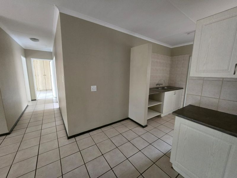 A functional kitchen area featuring built-in cabinetry, laminate countertops, and tiled flooring, leading into a hallway with built-in storage.
