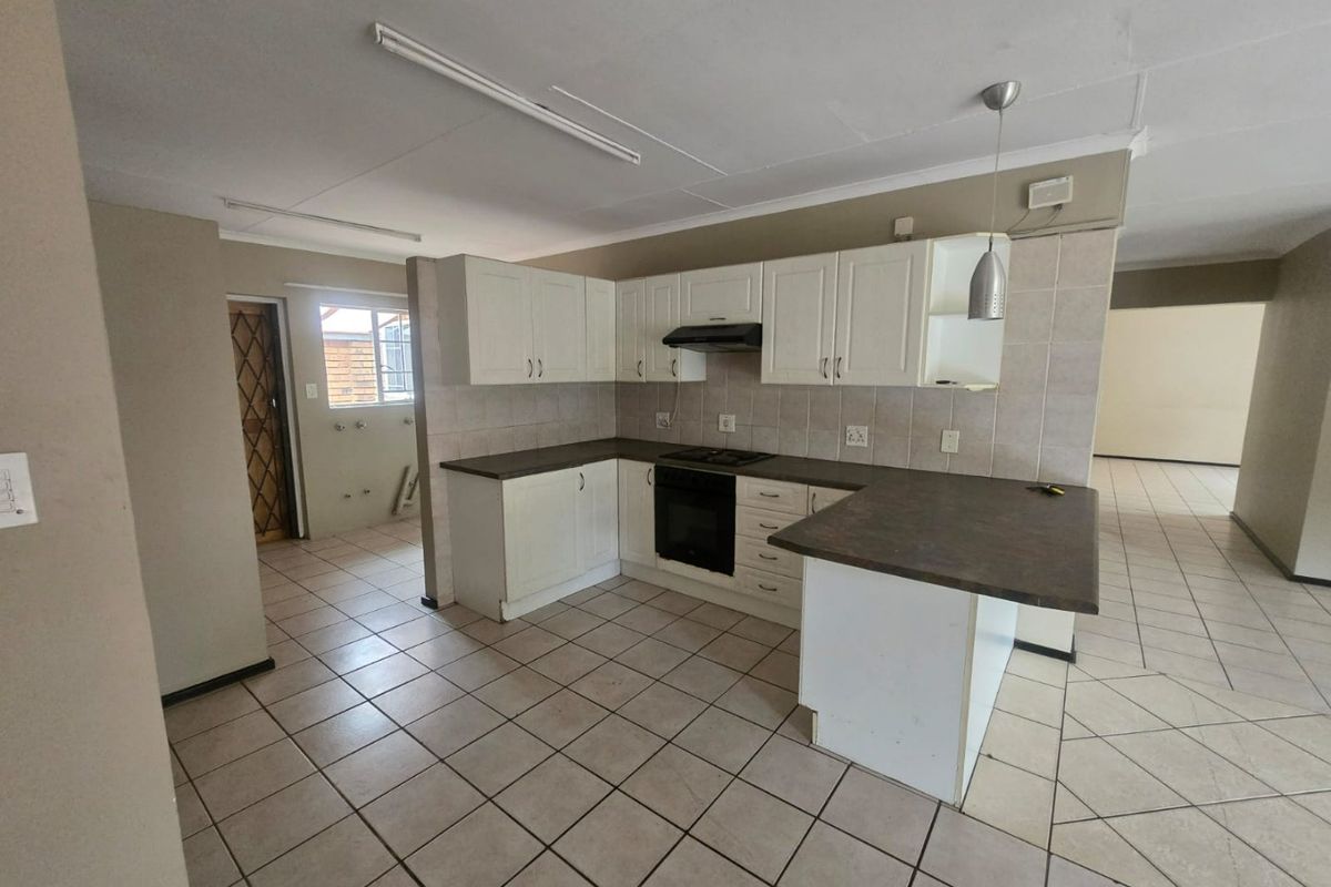 A functional kitchen featuring white built-in cabinetry, dark laminate countertops, an integrated oven and hob, and tiled flooring throughout.