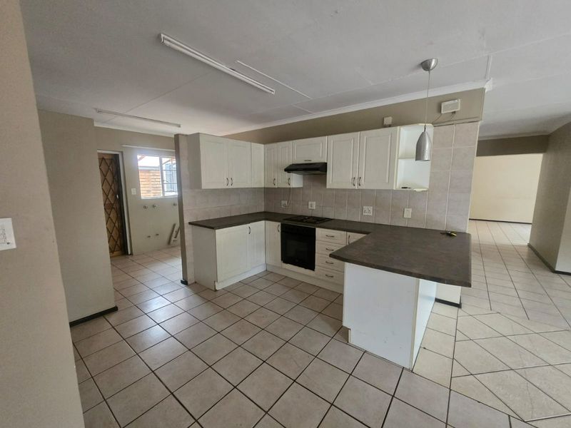 A functional kitchen featuring white built-in cabinetry, dark laminate countertops, an integrated oven and hob, and tiled flooring throughout.