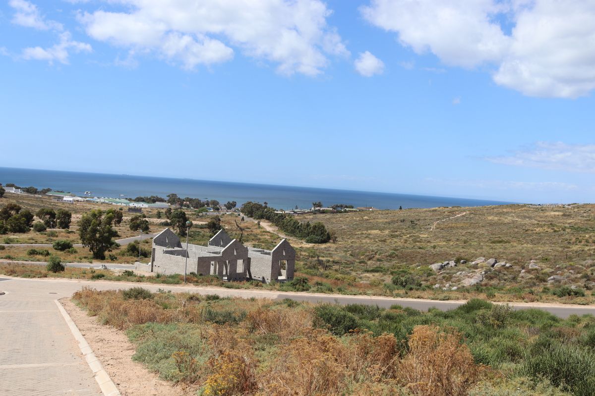 An elevated view of a vacant residential plot featuring an uncompleted masonry structure with scenic coastal and landscape views.