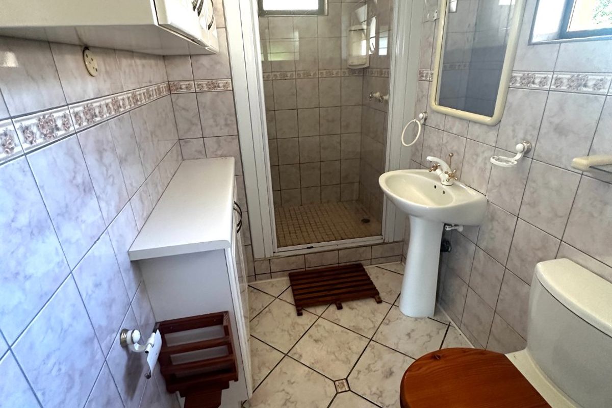 A functional bathroom featuring a shower enclosure, pedestal basin, and toilet, finished with neutral wall and floor tiles.