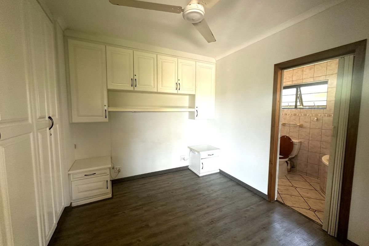 Bedroom featuring built-in cabinetry, ceiling fan, and laminate flooring, with an adjoining en-suite bathroom.