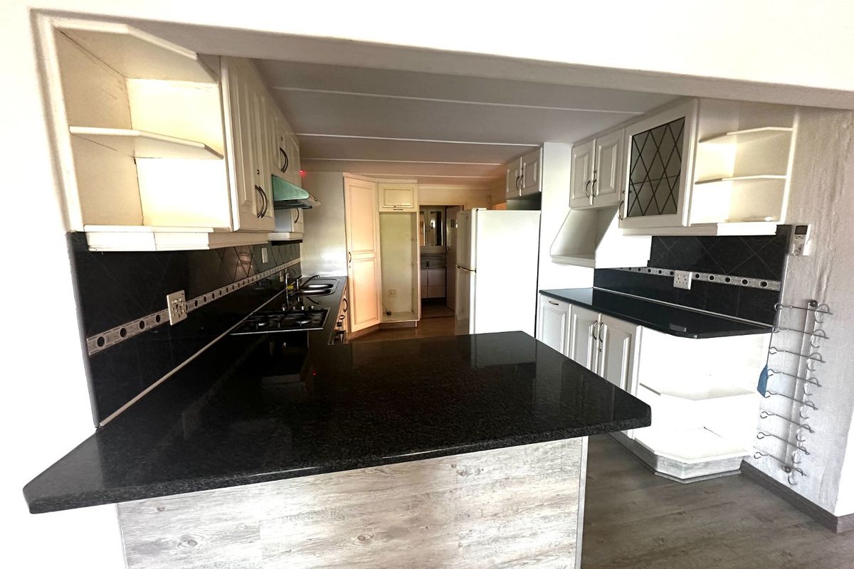 A functional kitchen featuring dark granite countertops, white cabinetry, a built-in hob, and an integrated layout with a breakfast bar.