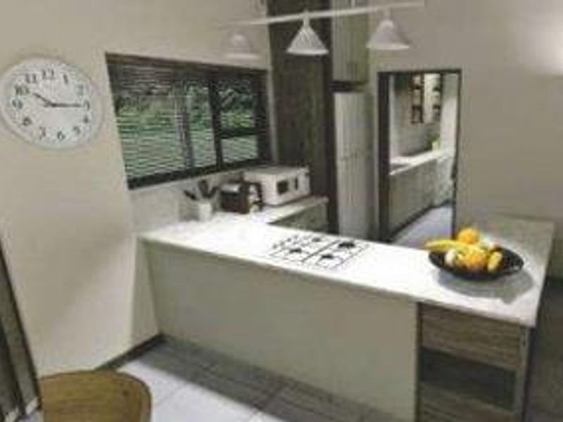 A functional kitchen featuring a breakfast bar, gas hob, stone countertops, and built-in cabinetry, with an adjacent scullery area visible.