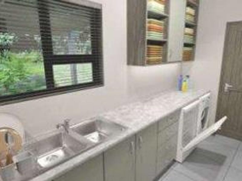 A functional laundry room featuring built-in cabinetry, a double stainless steel sink, ample counter space, and tiled flooring with natural light from the window.