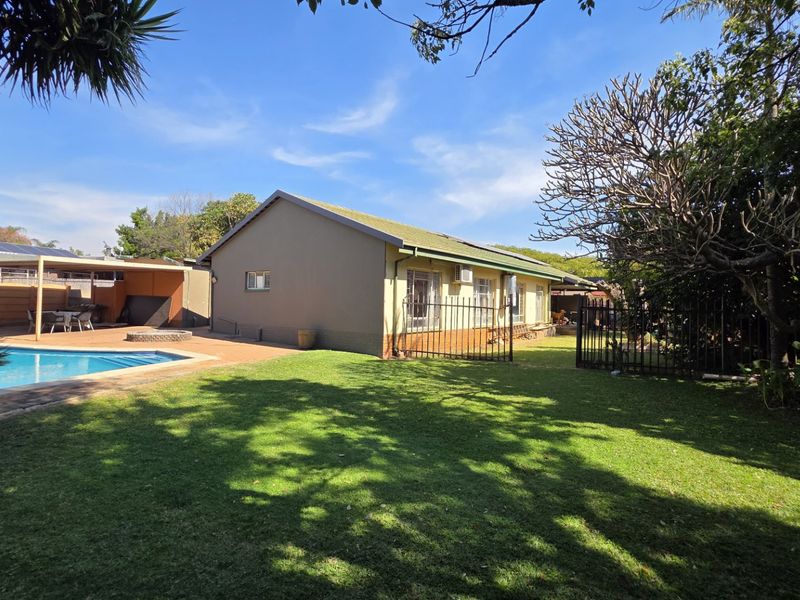 Rear view of the property featuring a swimming pool, paved patio area, and a well-maintained lawn with perimeter fencing.