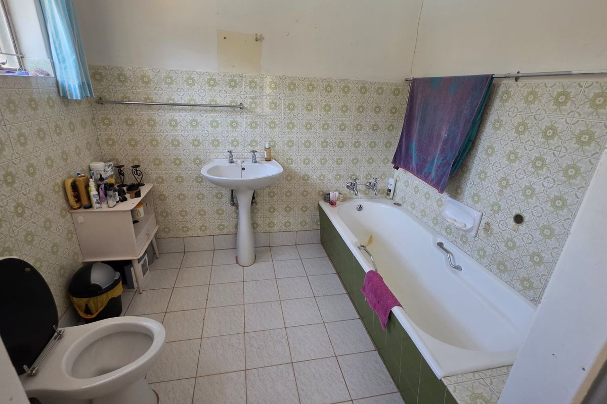 A dated bathroom featuring a pedestal basin, built-in bathtub, and original patterned wall tiling, offering significant potential for a modern renovation.