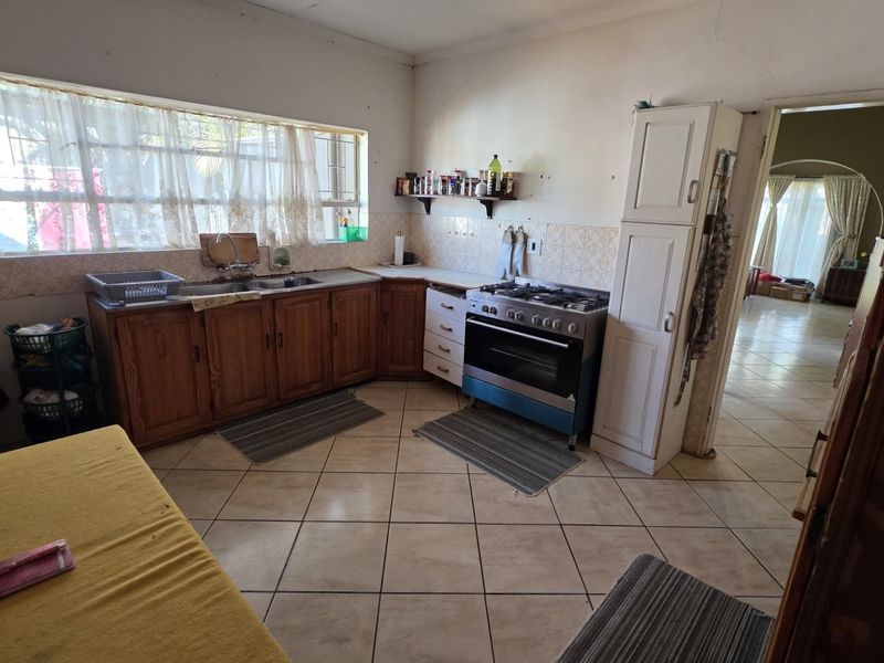 A functional kitchen featuring wooden cabinetry, a gas stove, double sink, and tiled flooring, offering potential for modernization and cosmetic updates.
