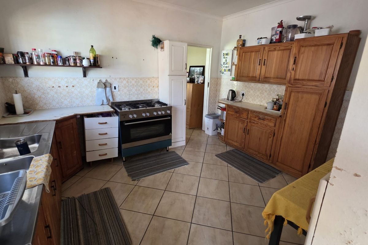 A functional kitchen featuring wooden cabinetry, a gas stove with oven, double sink, and tiled flooring with a tiled backsplash.