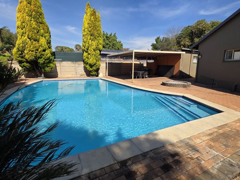Outdoor pool area featuring a swimming pool, paved patio, and a covered entertainment space with a built-in fire pit.