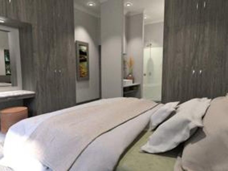 Modern bedroom featuring extensive built-in cabinetry, a dedicated vanity area, and direct access to an en-suite bathroom with recessed lighting throughout.
