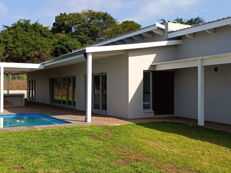 Rear exterior view featuring a modern home with a covered patio, built-in braai area, and a swimming pool set within a landscaped garden.