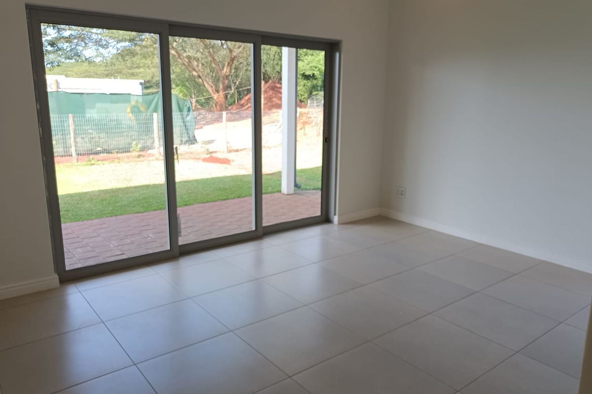 A bright, empty living room featuring large sliding glass doors that open onto a paved patio and garden area, finished with neutral floor tiles.